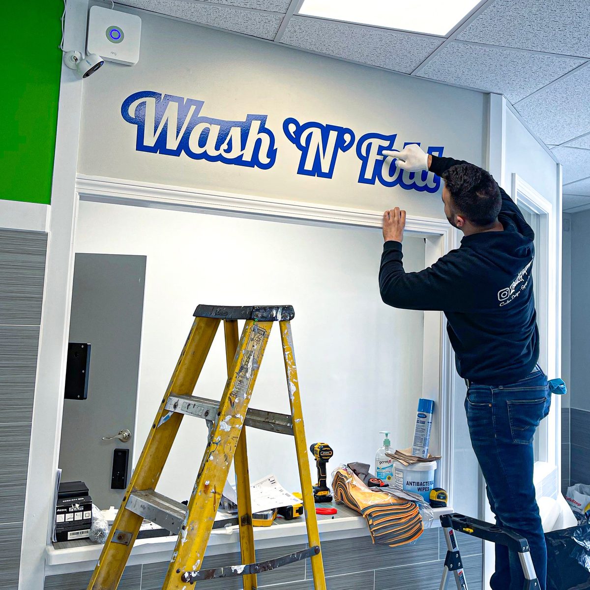 Charbel Saade installing Wash 'N' Fold wall lettering from a ladder