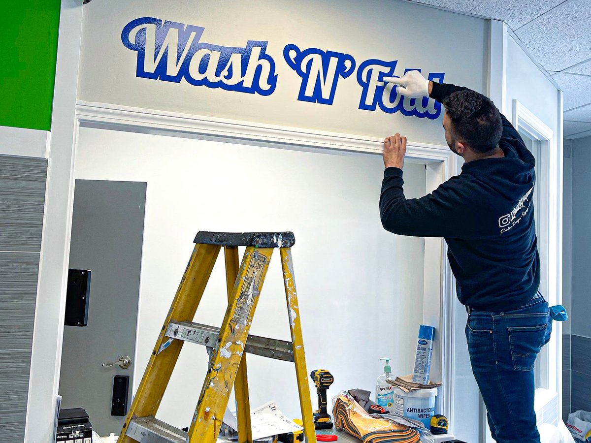Charbel Saade installing Wash 'N' Fold wall lettering from a ladder