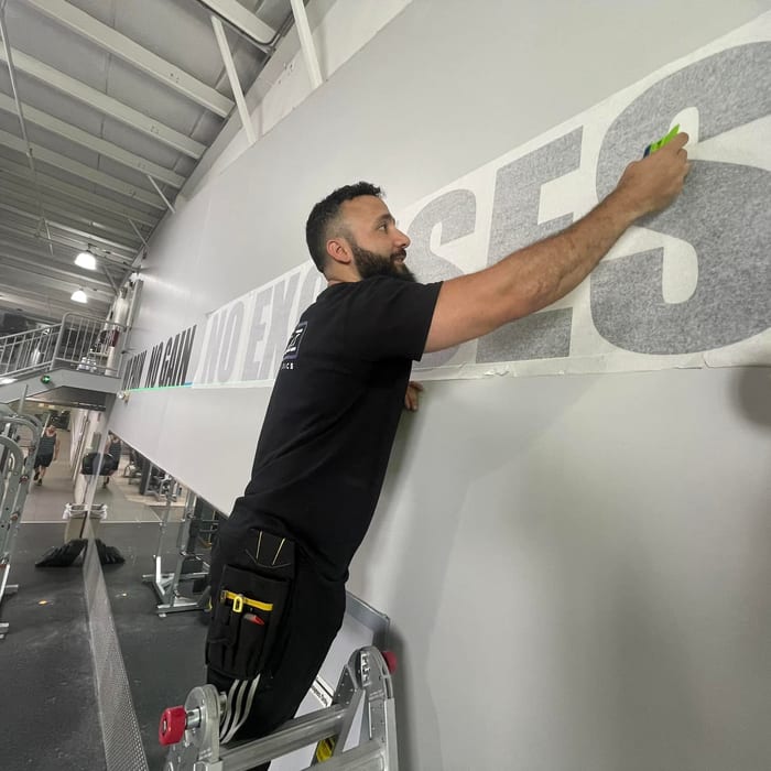 Joe Saade installing black wall lettering at The Workout Club in Londonderry, NH