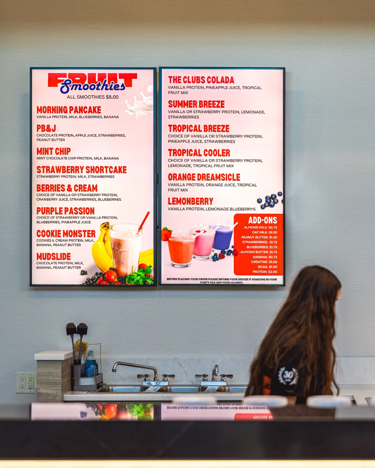 Two vertical menu screens above The Workout Club's smoothie bar, showing fruit smoothies and add-ons